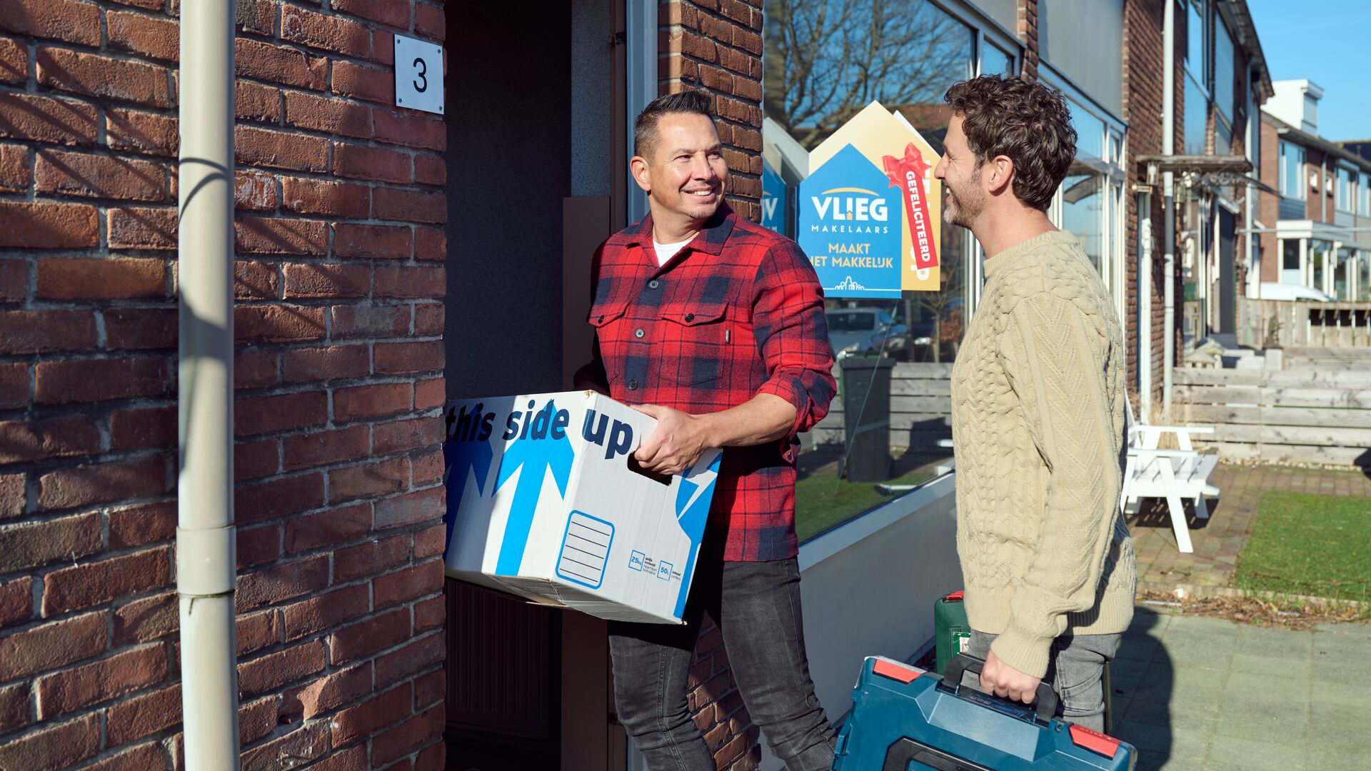 Twee mannen met verhuisdoos en gereedschapskist bij hun nieuwe woning